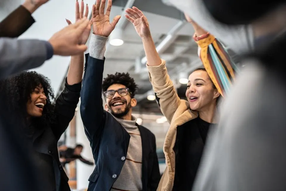 A team raising hands together in a modern office, symbolizing collaboration and success in technology entrepreneurship