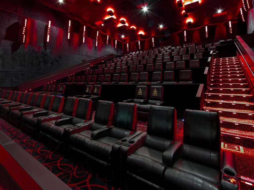 Interior view of AMC movie theater featuring luxurious black leather recliner seats and ambient red lighting, showcasing a premium movie-going experience 