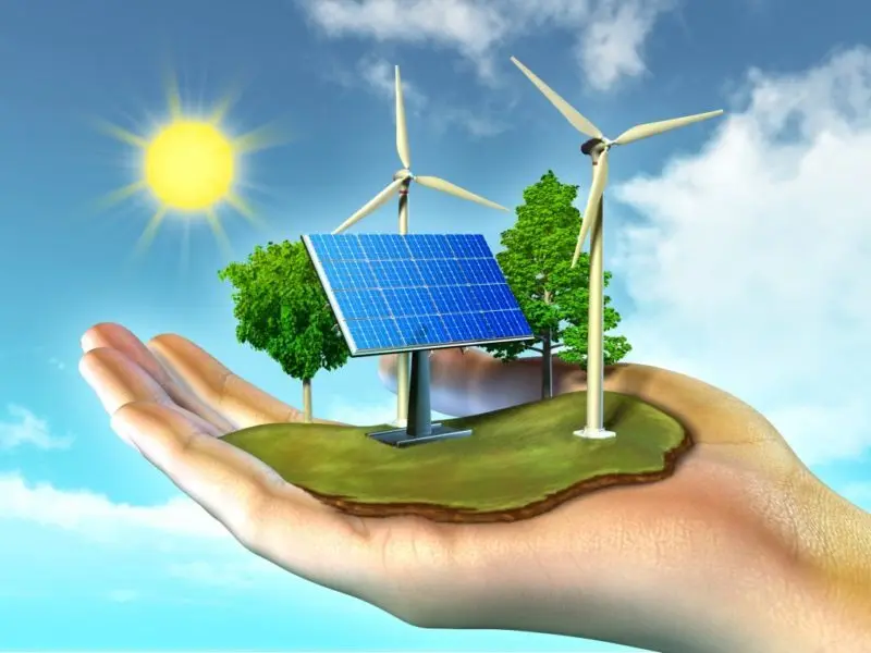 A hand holding wind turbines and a solar panel set against a sunny sky, symbolizing renewable energy and sustainable power generation 
