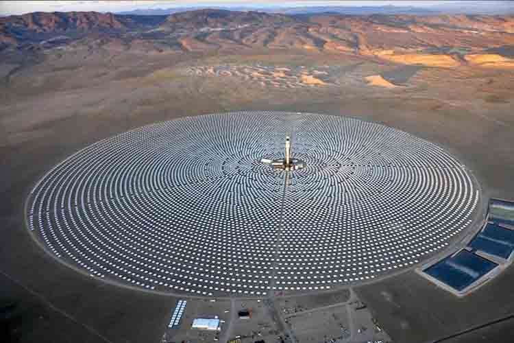 Aerial view of a large circular solar power plant with central tower and thousands of mirrors in a desert landscape 