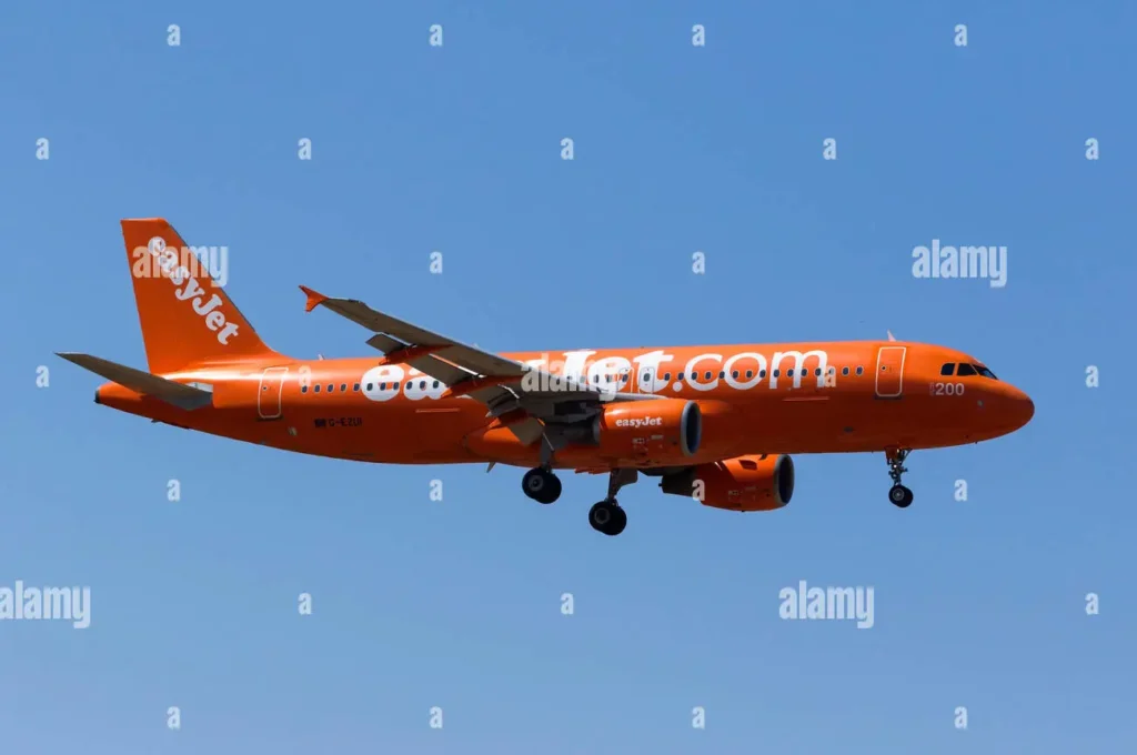 An EasyJet airplane in bright orange livery flying against a clear blue sky with landing gear extended