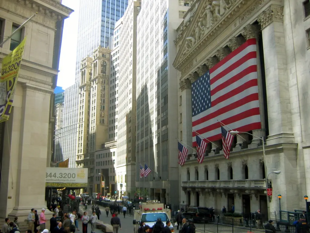 Wall Street financial district showing the New York Stock Exchange building with American flags and busy street activity 